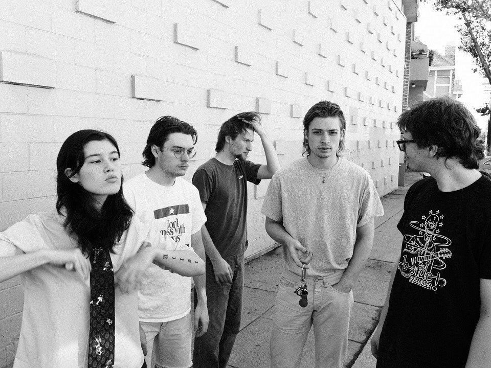 The five members of Disq in front of a cement block wall.