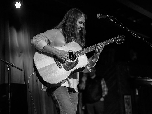 Ben Majeska with an acoustic guitar on stage.