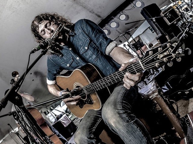 A person on stage with guitar and harmonica.