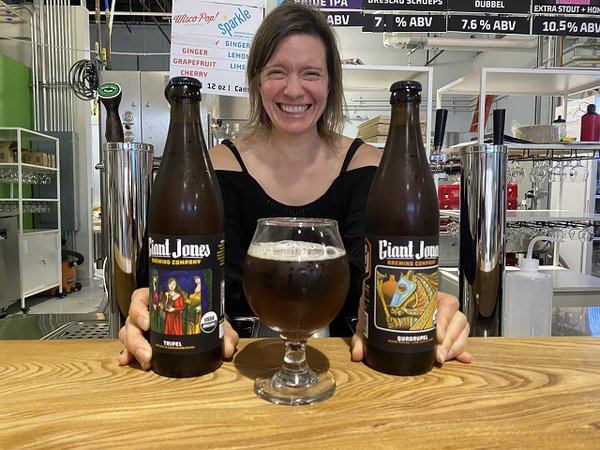 Erika Jones behind the bar at Giant Jones with a glass of a Belgian and two bottles.