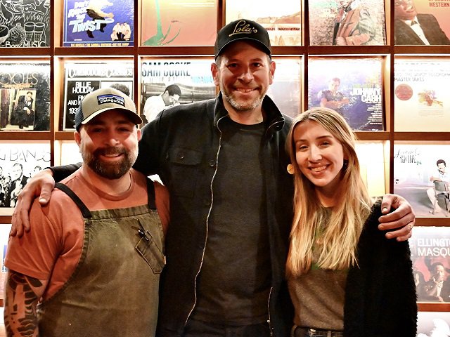 Evan Dannells, Matt Gerding and Tori Gerding in front of a wall of LP covers that are staged attractively with lighting.