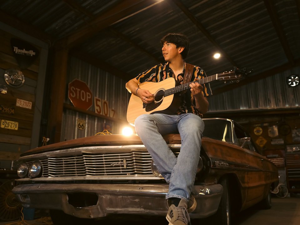 Wyatt Flores and guitar sitting on a 1960s Ford Galaxie.