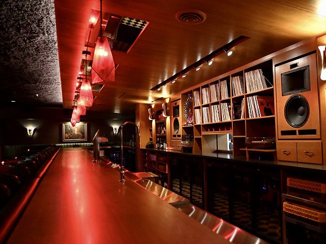 Bar interior with red lights shining down on bar and vinyl records behind.