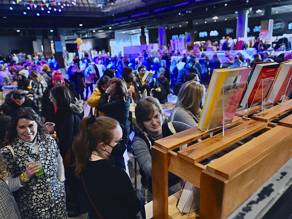 Crowded room of people with books in the foreground.