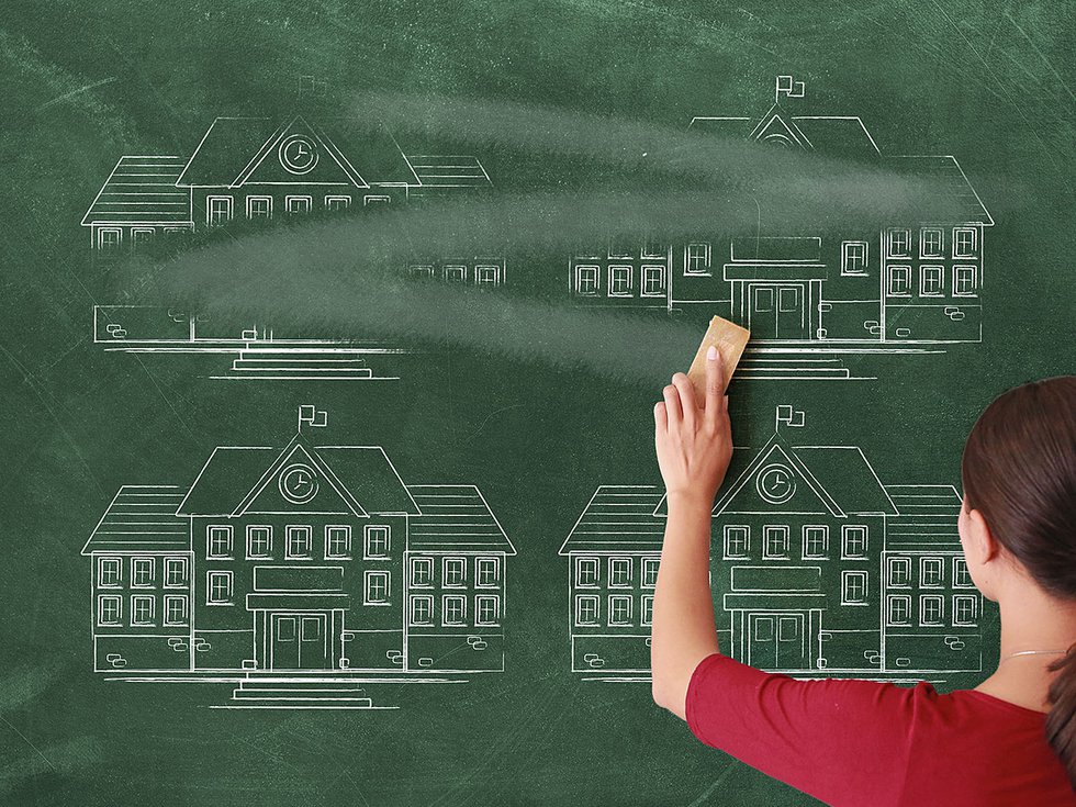 A woman erasing drawings of school buildings off a chalkboard.