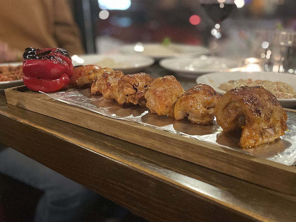 Pieces of chicken lined up on a narrow serving tray with a charred red pepper at one end.