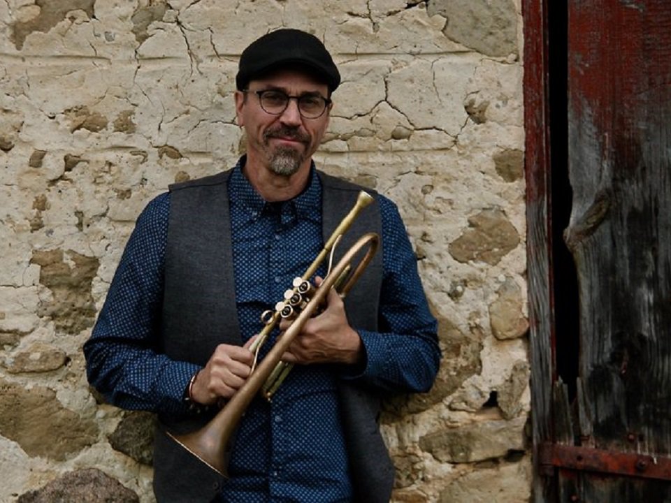 Dave Cooper and trumpet in front of a stone wall.