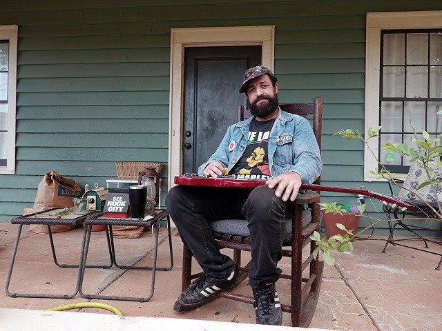 Lee Bains on a porch with a guitar.