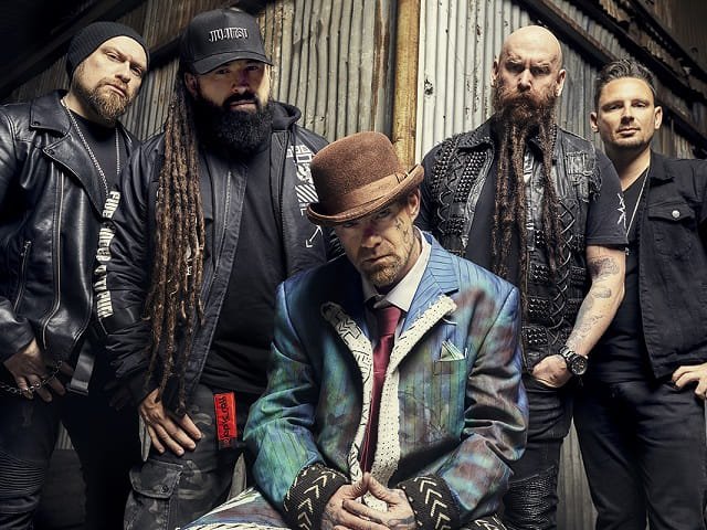 The five members of Five Finger Death Punch in front of a corrugated metal wall.