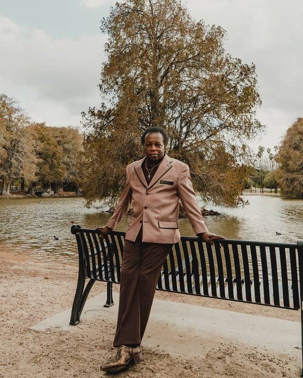 Lee Fields leans on a park bench by a pond.