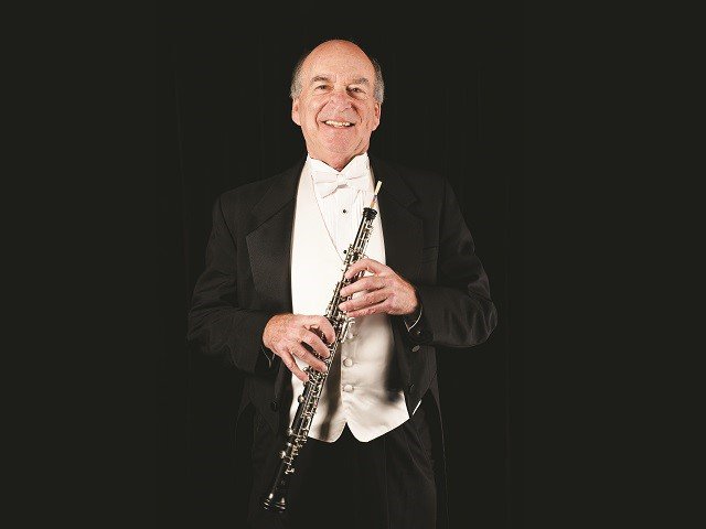 A man with an oboe in front of a dark background.