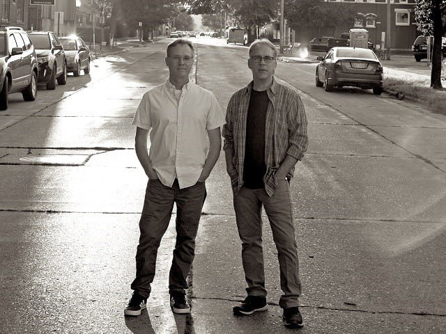 Two brothers stand on a street.