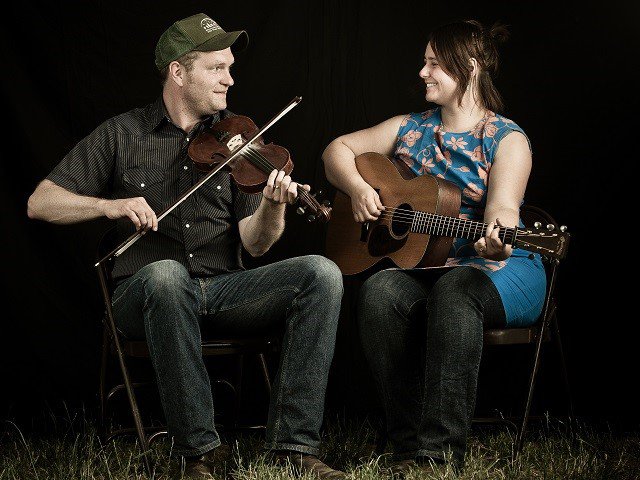 A man with a fiddle and a woman with a guitar.