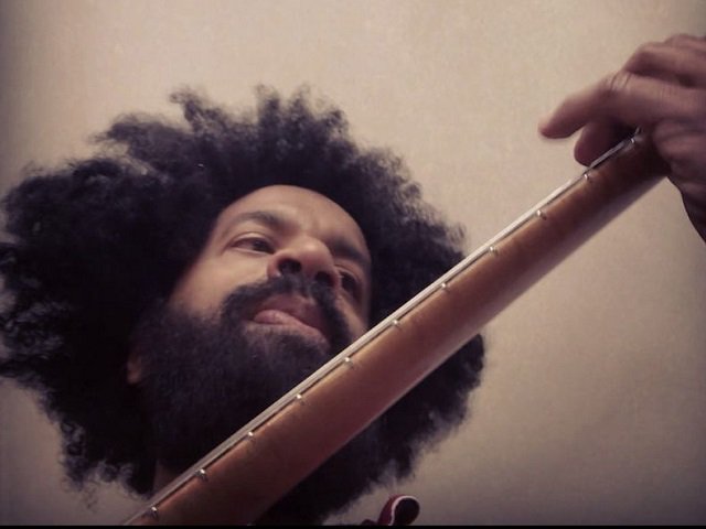 A man from the perspective of under a guitar neck.