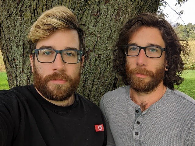 A close up of two men in front of a tree.