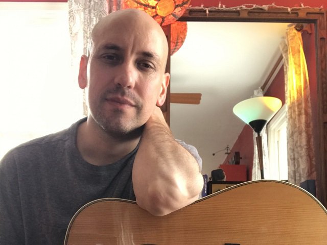 A man leans on a guitar.