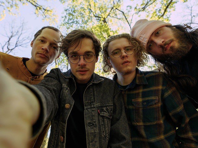 The camera looks up at four people framed by tree and sky.