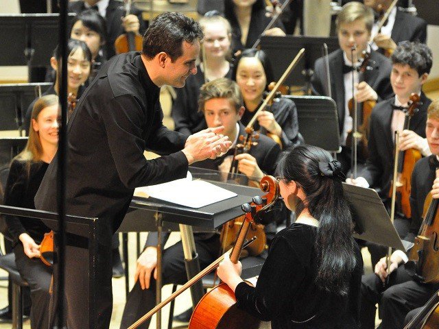 A group of young orchestsral players around a conductor.