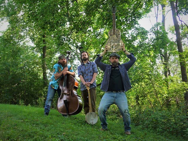 A trio of people with instruments in a glade.