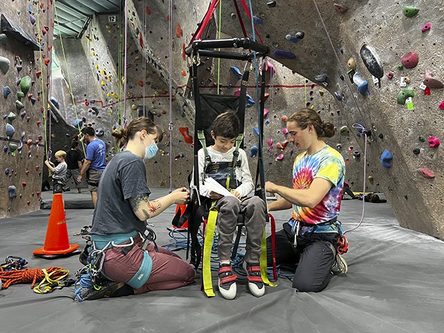 Two adults with a child in an adaptive climbing chair