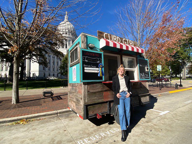 Woman in front of Curd Girl food cart on Capitol Square on fall day