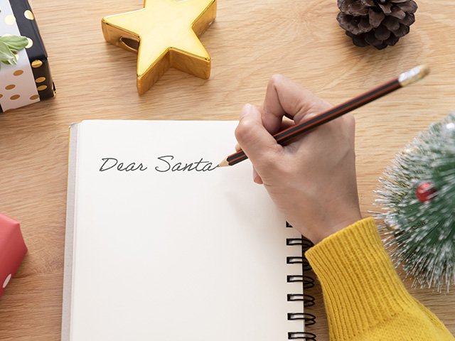 A hand is writing Santa a letter on a notebook page.