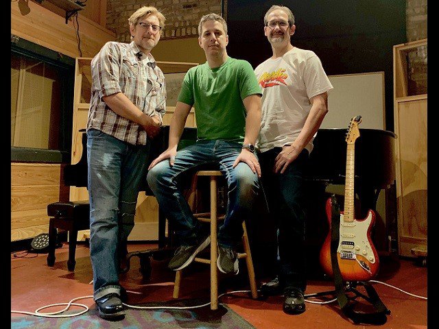 A three-piece band in a studio space.