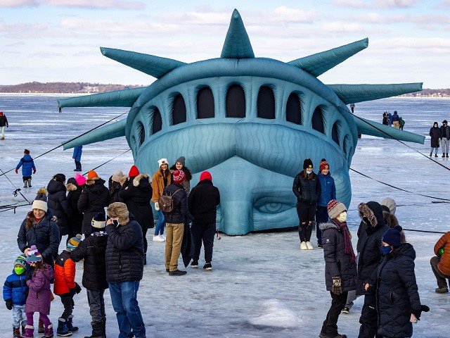 A facsimilie Lady Liberty rises from the ice of Lake Mendota, surounded by people.