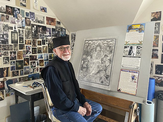 Berndt, with white beard and black hat, sits at studio easel surrounded by drawings.
