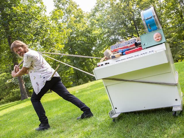 A person pulling a keyboard instrument across a lawn.