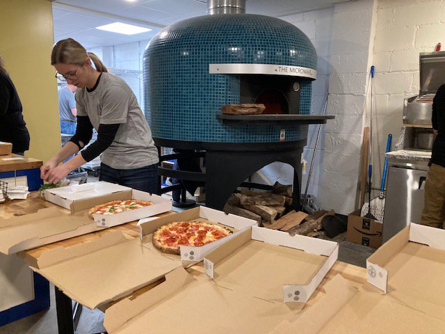 A person putting toppings on pizza and a pizza oven.
