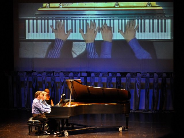 Two piano players at a grand piano on stage.