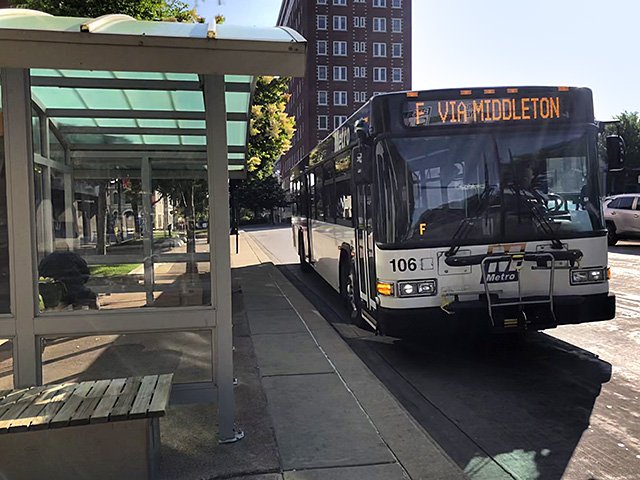A Madison Metro bus pulls up to a bus shelter.