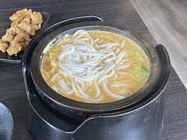 Coconut red curry noodle soup in a black bowl.