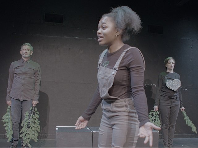 Two actors playing trees observe another actor at center stage.