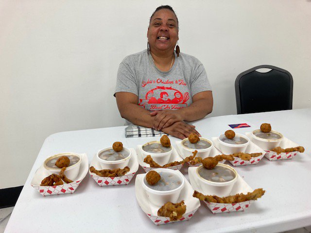 Nisa Carter sitting at a table with samples of her gumbo, hush puppies and fried chicken wings.