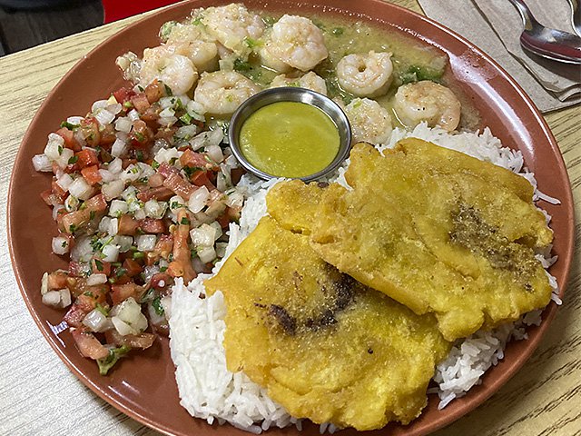 A plate with garlic shrimp, rice, fried plantains and salad.