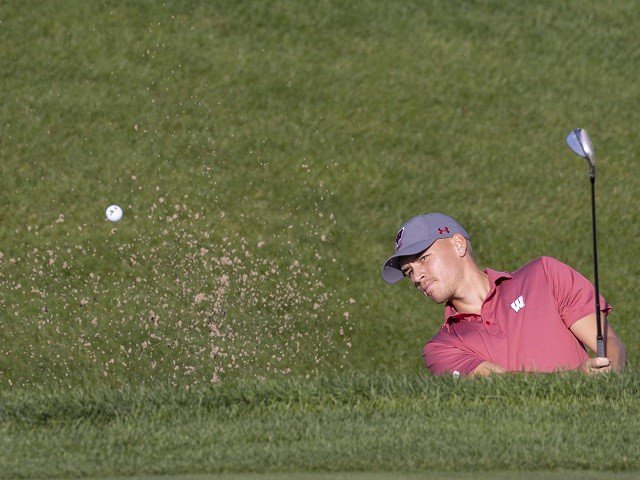 A golfer knocks the ball from a sand trap.