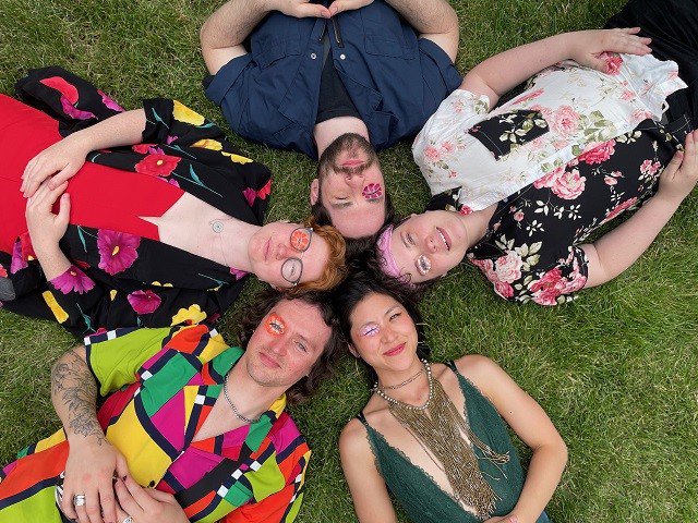 Five people laying in the grass in a circle.