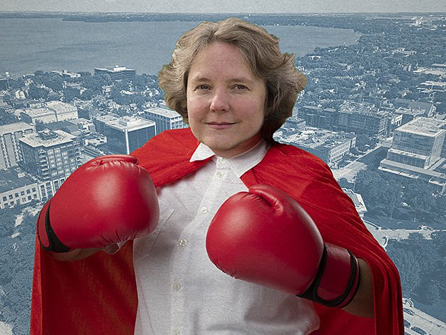 Madison Mayor Satya Rhodes-Conway with boxing gloves in front of a backdrop of Madison.