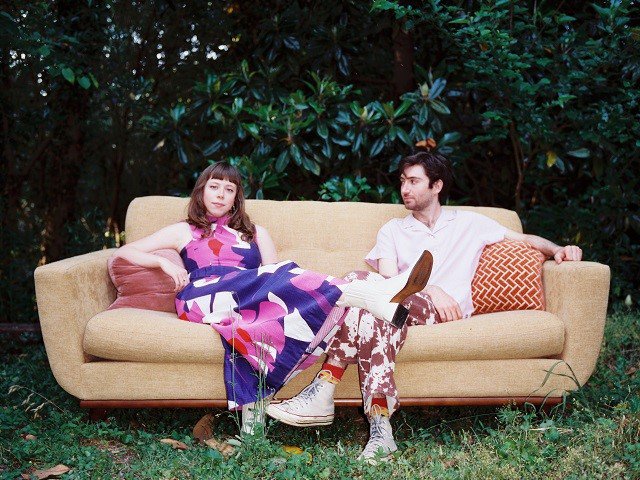 Two people sitting on a couch in the woods.
