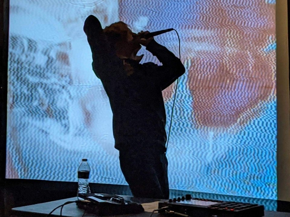 A person on the mic in front of a video projection.
