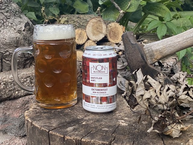 A beer in a glass, its can and an axe on a tree stump in a fall beer scene.