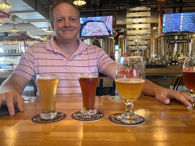 John Russell behind the bar at Lone Girl with glasses of three different kinds of Belgian beer.