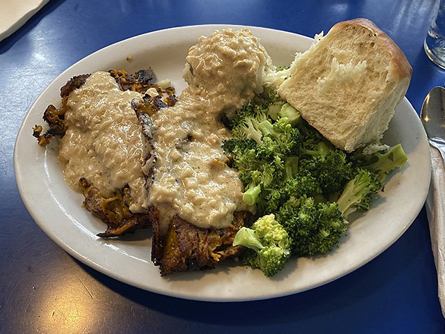 The veggie loaf of the gods on a white plate on the blue table at Monty's Blue Plate. Plate includes broccoli and mashed potatoes.