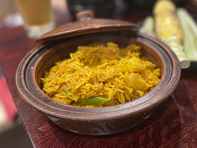 Lovely yellow rice in this vegetarian biryani in a brown lidded serving dish.