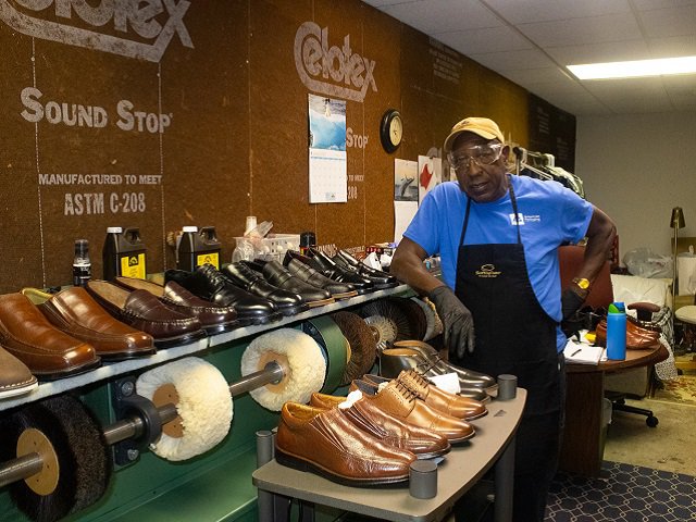 Tosh Washington stands in his show with two rows of men's shoes.