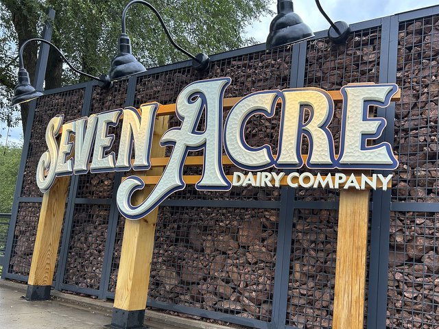 The Seven Acre sign, with a lot of wood stacked up behind it.