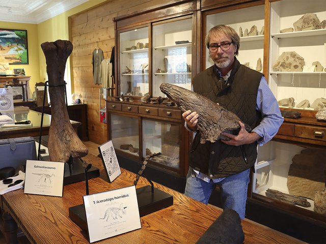 Man holding a large dinosaur bone in front of glass display cases.