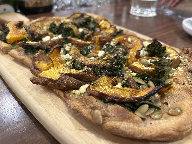 A tarte flambee, which looks like a flatbread pizza, on a wooden serving platter.